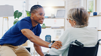 Male caregiver smiling and putting his hand on the arm of an older woman in a wheelchair in a home