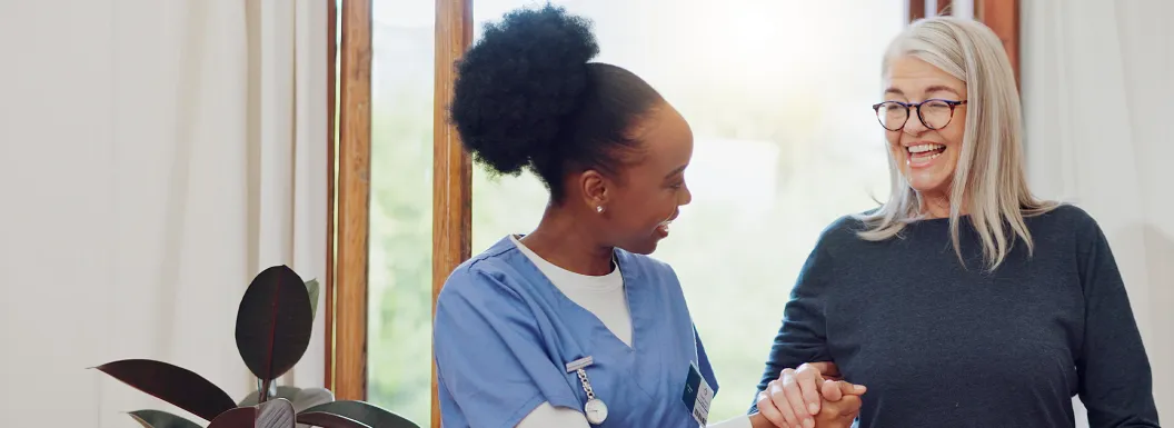 Caregiver smiling and holding the hand of an elderly woman to help assist her walking