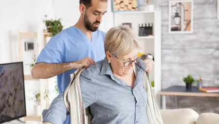Caregiver helping elderly woman put on a shirt
