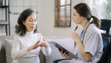 Woman talking to a Community Health Workers who is listening and holding a clipboard, writing down notes