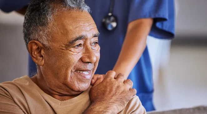 Elderly man smiling and holding the hand of his caregiver on his shoulder