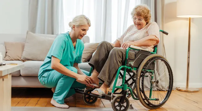 Nurse helps an elderly woman with slippers and in a wheelchair at home