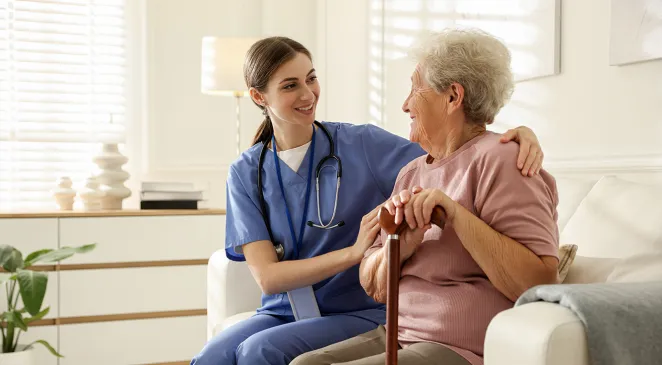 Caregiver supporting senior woman on sofa