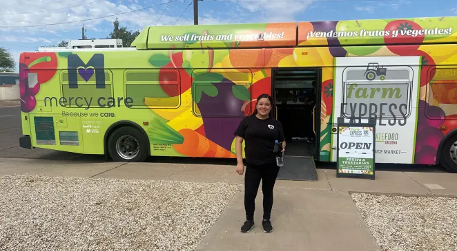 Home Assist Health employee standing in front of a bus with a Mercy Care and Farm Express wrap with fruit graphic