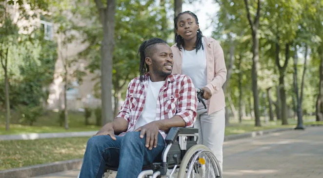 Community Health Worker pushing wheelchair with male patient in park