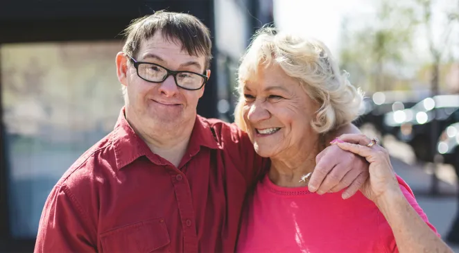 Middle aged autistic man smiling with his arm around an elderly woman smiling