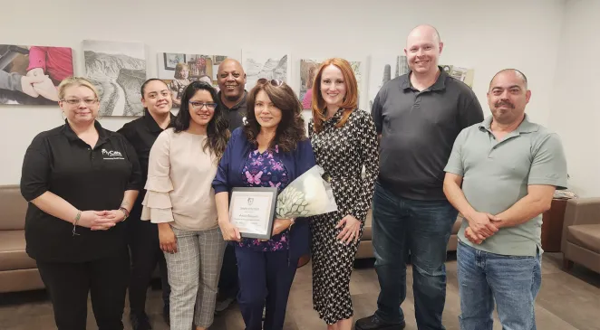 Home Assist Health team member posing together around a woman holding a certificate for "Caregiver of the Month" in the Home Assist Health office