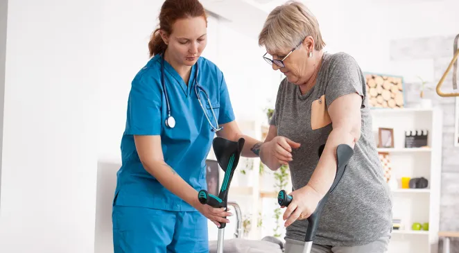 Caregiver assisting elderly woman putting on forearm crutches