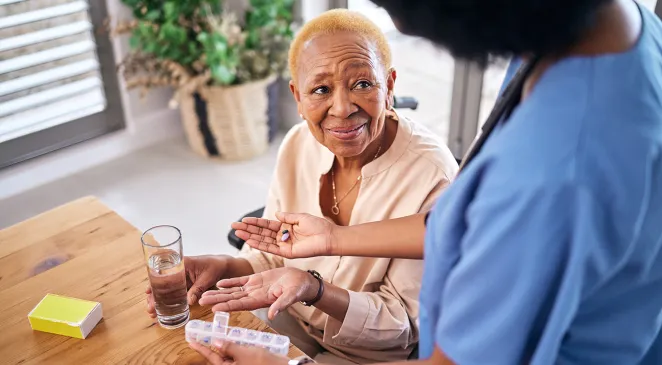 Nurse smiling and giving old woman pills in home with water for healthcare, wellness and support