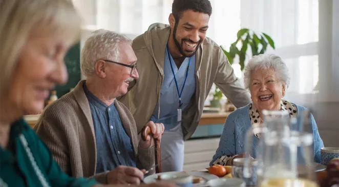 Young man caregiver smiling with a group of seniors smiling over breakfast