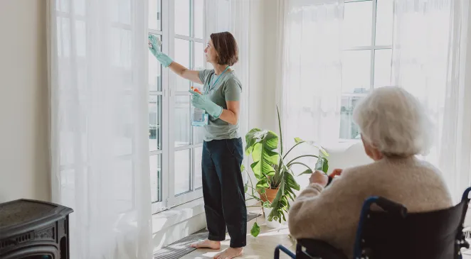 Senior woman in a wheelchair watching her caregiver clean windows