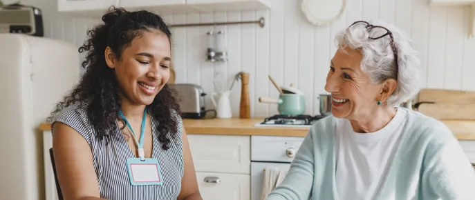 Senior lady having fun building a puzzle at a kitchen table with a caregiver