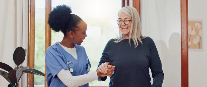 Caregiver smiling and holding the hand of an elderly woman to help assist her walking